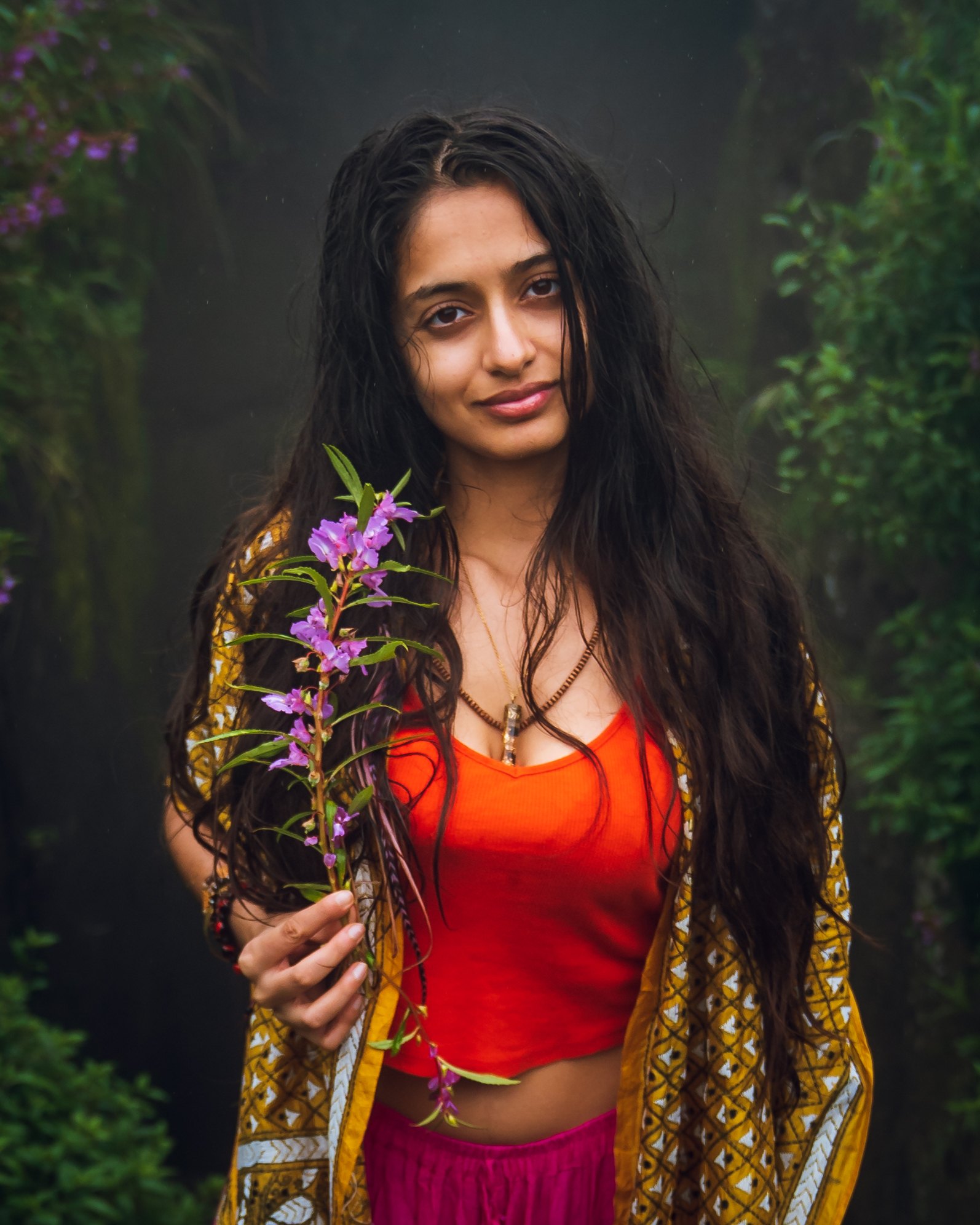 Kamya holding a stem of wild purple flowers in a misty forest