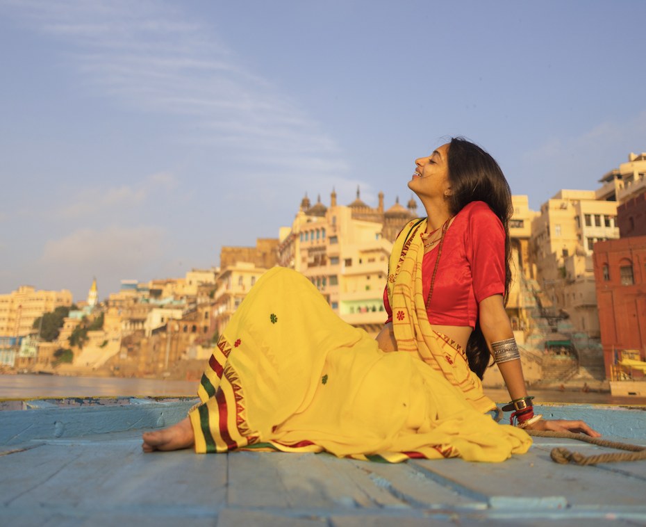Kamya in a yellow sari on a boat on the Ganga, the ghats of Kashi behind her